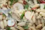 Ensalada templada de judías blancas con rodajas de rábano y filetes de sardina.